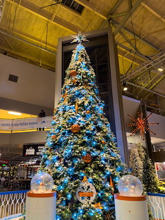 Tall Christmas tree decorated with blue and gold ornaments in an indoor setting