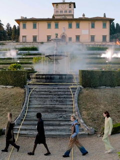 Three people walking past a large tiered fountain in the gardens of an Italian Renaissance villa