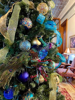 Christmas tree with blue ornaments, gold ribbons, peacock feathers, and colorful lights in decorated room