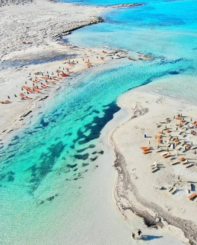 Aerial photo of turquoise shallow waters and white sandy beach with sunbathers in Crete, Greece