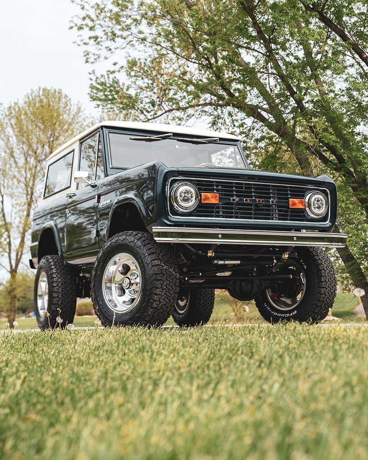 Dark green classic Ford Bronco 4x4 SUV on grass with trees in background