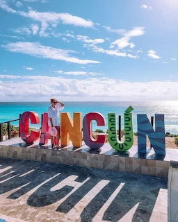 Colorful Cancun sign on a seaside promenade with ocean and blue sky in the background.