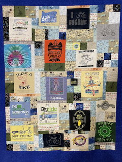 Patchwork quilt made from bicycle-themed t-shirts with various cycling logos and graphics on blue background