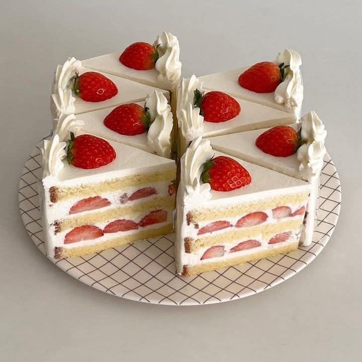 Eight triangular strawberry shortcake slices with whipped cream and fresh strawberries on a wire rack