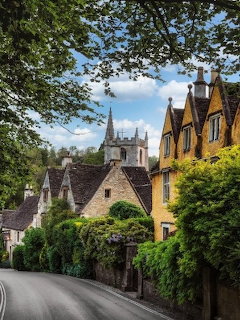 Village road with stone cottages, hedges, and a church tower in the Cotswolds