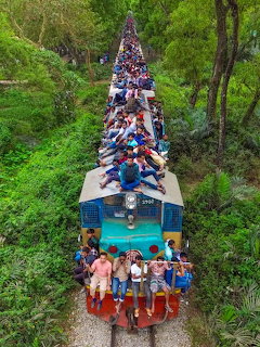 Aerial view of a crowded train with people sitting on the roof moving through dense green trees
