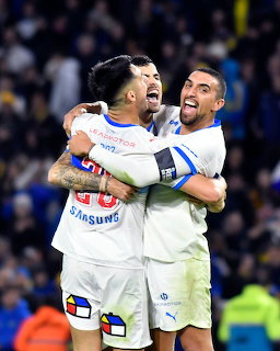 Three soccer players in white uniforms hugging and celebrating during a match