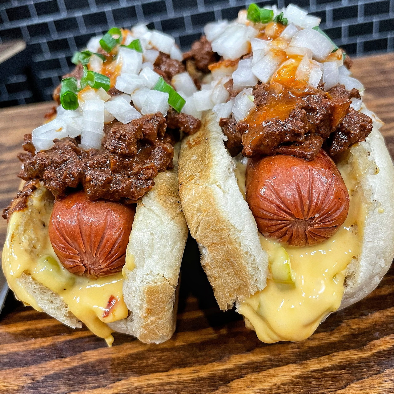 Two chili dogs with meat, cheese, onions, and peppers on a wooden serving board