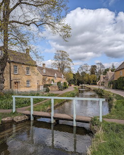 White wooden footbridge over calm river in English village with stone cottages and blue sky