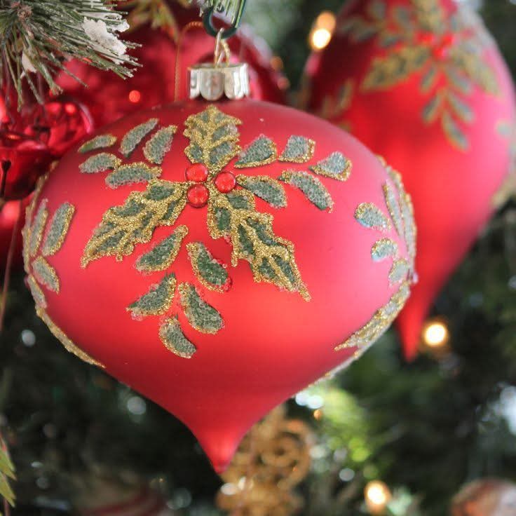Red teardrop Christmas ornament with gold snowflake design on evergreen tree with blurred lights