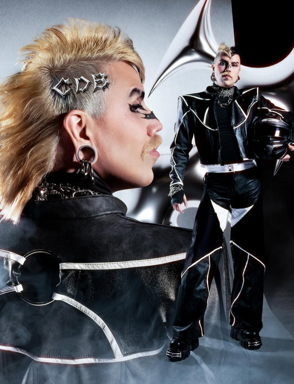 Two models in black leather punk fashion outfits with bold hair and makeup in a stylized editorial shoot.