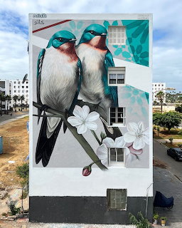 Street art mural of two birds on a building wall with white flowers