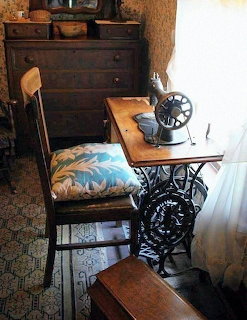 Vintage treadle sewing machine with cast iron base next to a wooden chair with floral cushion