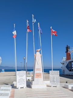 Monument with flagpoles and colorful flags on a sunny harbor waterfront in Thassos, Greece