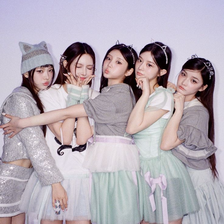 Five young women posing together in pastel dresses and winter accessories in a studio