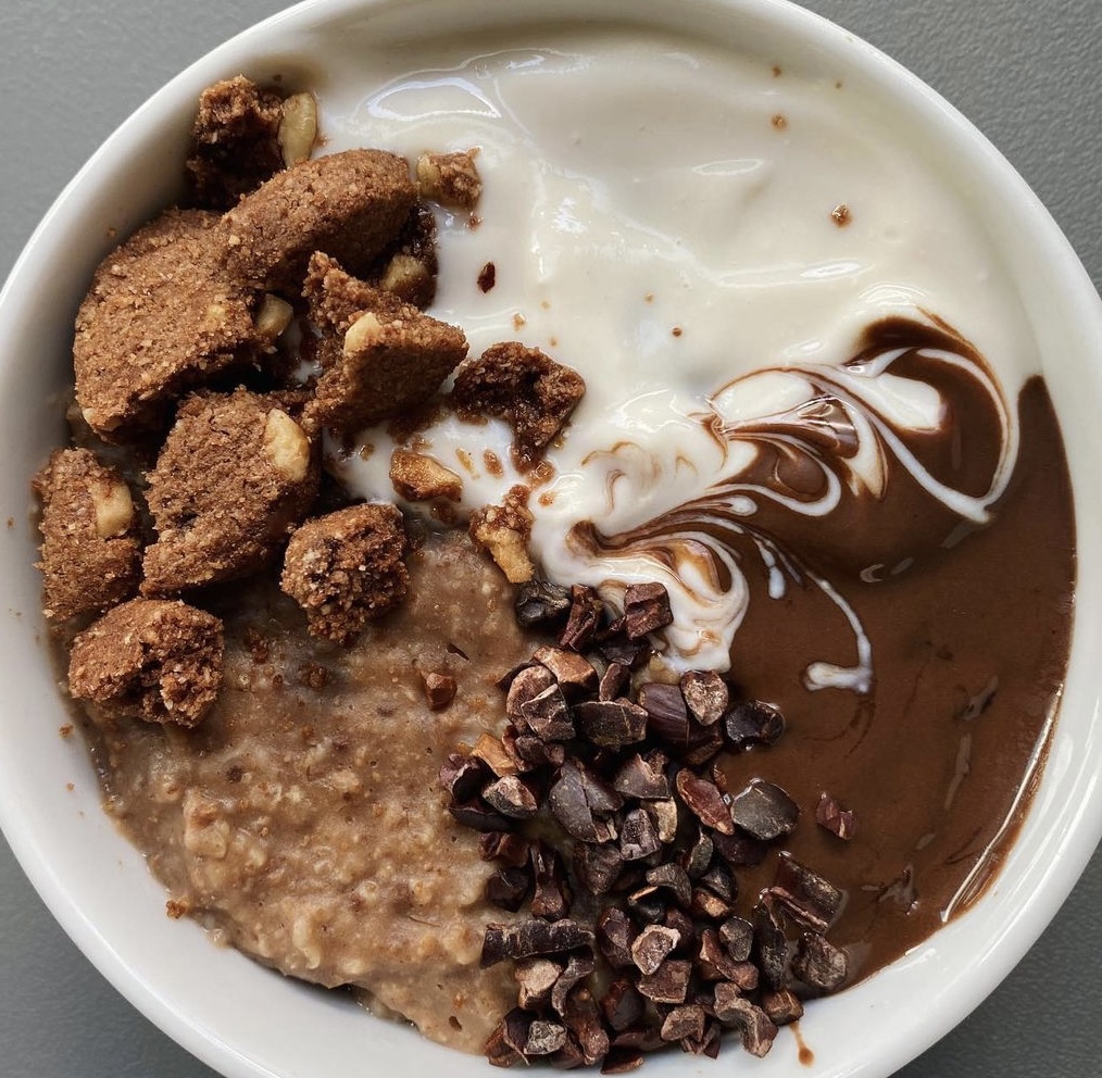 Bowl of oatmeal topped with yogurt, chocolate spread, cereal chunks, and cacao nibs