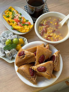 Overhead view of Korean food including rice cakes with dates, corn soup, omelette, and fruit on a table