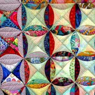 Cathedral window quilt pattern with multicolored curved fabric pieces forming circular and diamond shapes