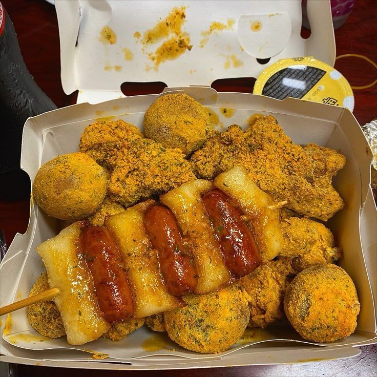 Takeout box of Korean street food with fried chicken, skewered rice cakes, sausages, and seasoned snacks