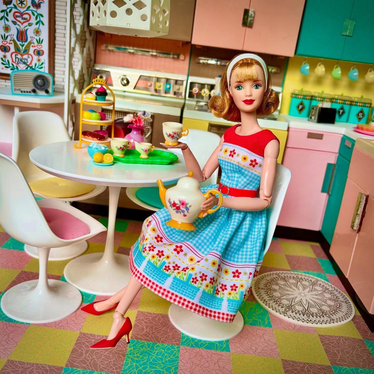 Blonde fashion doll seated in a colorful retro kitchen with a teacup and a fluffy white cat