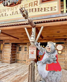 Costumed bear character waving in front of Country Bear Jamboree log cabin attraction entrance