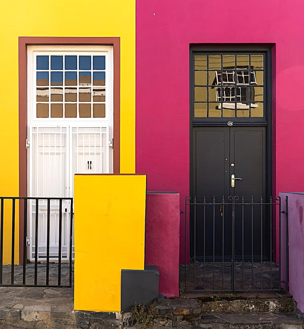Two adjacent doors on brightly painted yellow and pink walls with decorative windows and black iron railings