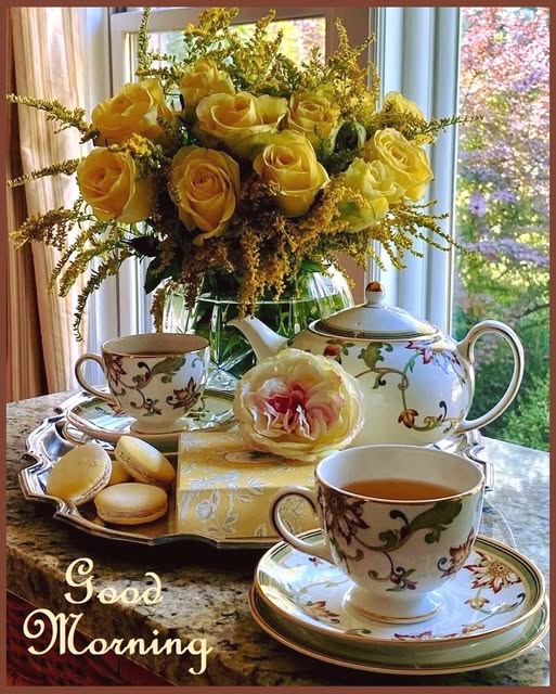 Floral tea set with teapot and cups on a tray next to yellow roses bouquet by a window