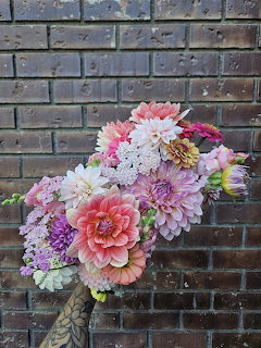 Colorful bouquet of mixed flowers in a patterned vase against a dark brick wall
