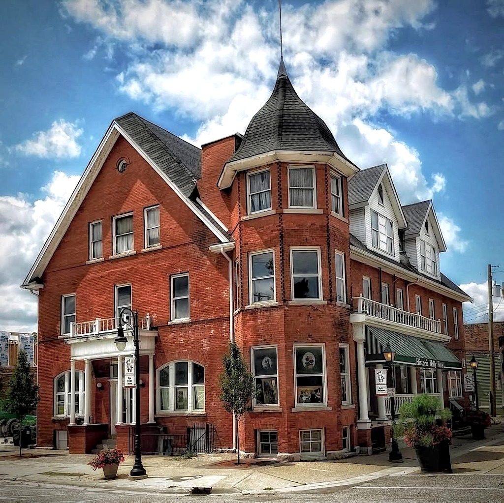 Historic red brick corner house with turret and wraparound porch under blue sky with white clouds