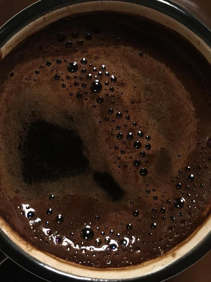 Top view of black coffee in a cup with dark crema and scattered bubbles