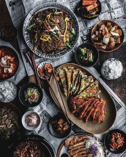 Overhead flatlay of diverse gourmet dishes including grilled meat, noodles, and vegetables on rustic table