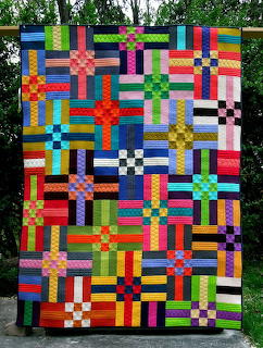 Colorful quilt with cross and checkerboard patterns in many bright fabric colors displayed outdoors