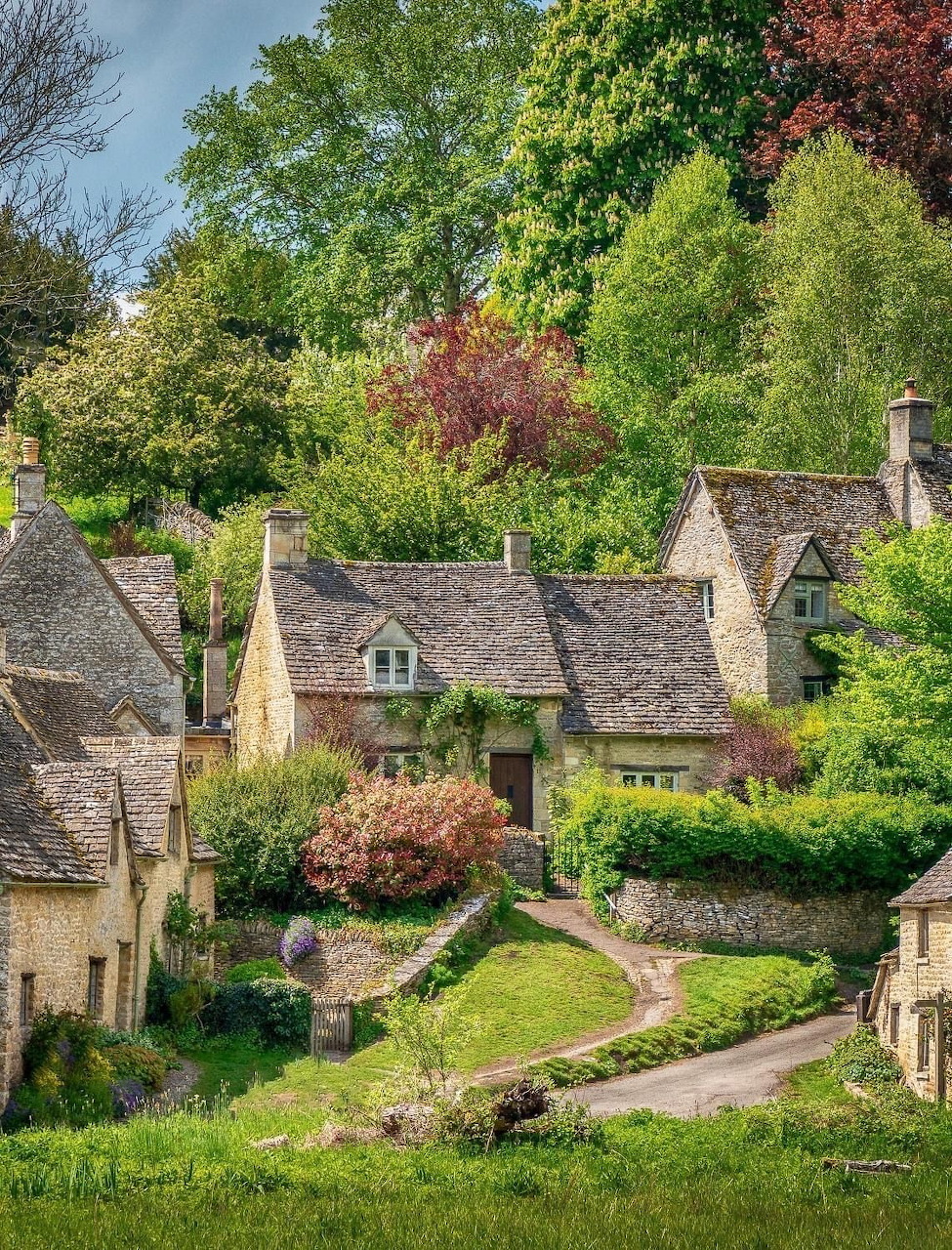 Stone cottages with slate roofs on a green hillside with blooming trees and gardens