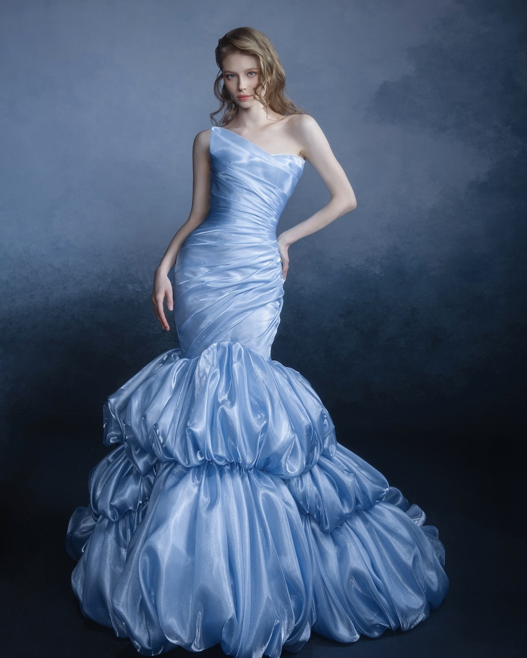 Woman posing in a light blue ruffled bridal gown against a dark studio background
