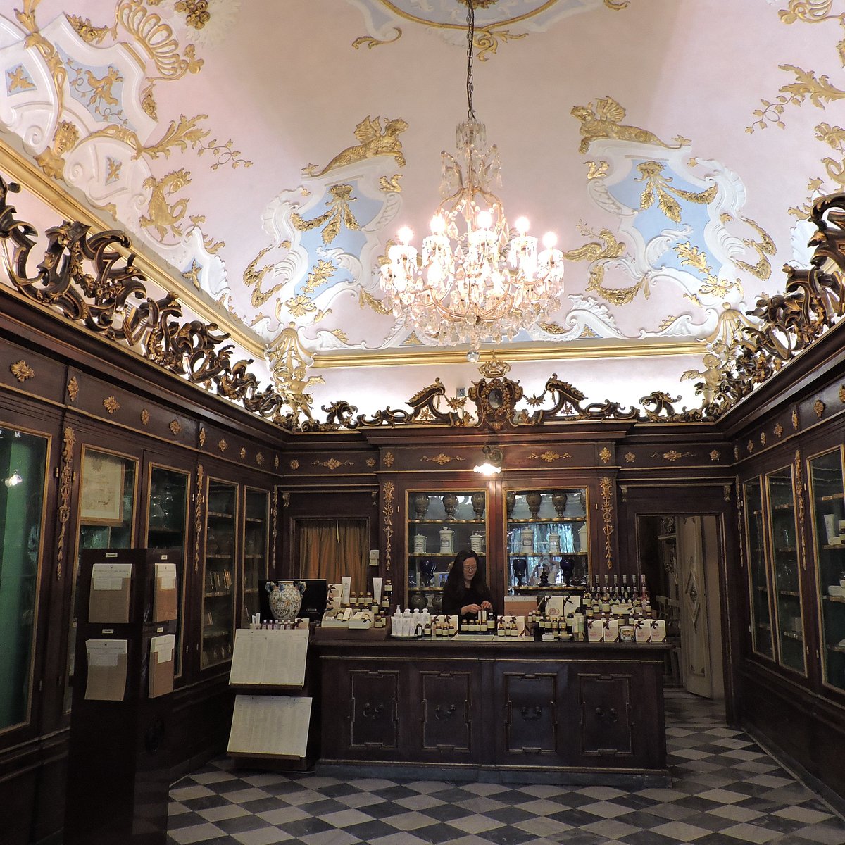 Elegant historic pharmacy interior with painted vaulted ceiling, chandelier, wooden display cases and marble floor