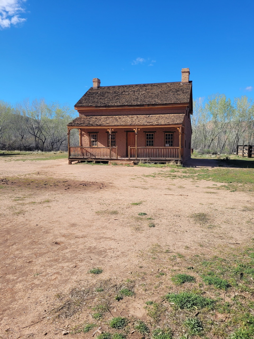Abandoned two-story brick farmhouse with front porch in a ghost town with bare dirt yard and trees