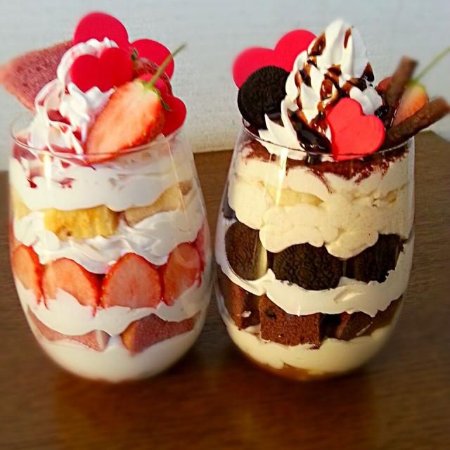 Two glass jars filled with layered desserts, one with strawberries and one with chocolate, topped with whipped cream and hearts
