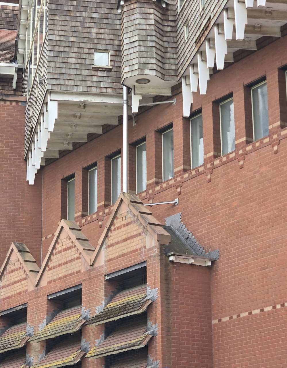 Modern building facade with red brick, angular balconies, and cylindrical glass tower detail