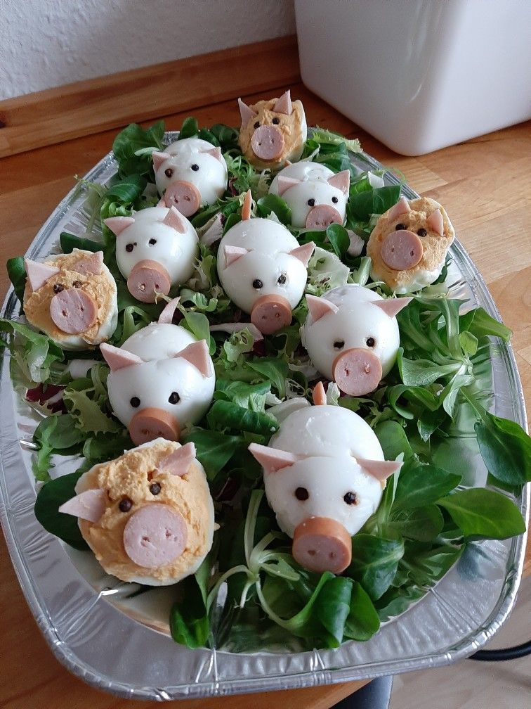 Hard-boiled eggs decorated to look like pigs sitting on green salad leaves on a silver platter