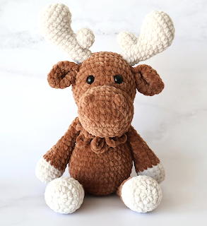 Brown and white crocheted amigurumi moose toy with antlers sitting on a marble surface