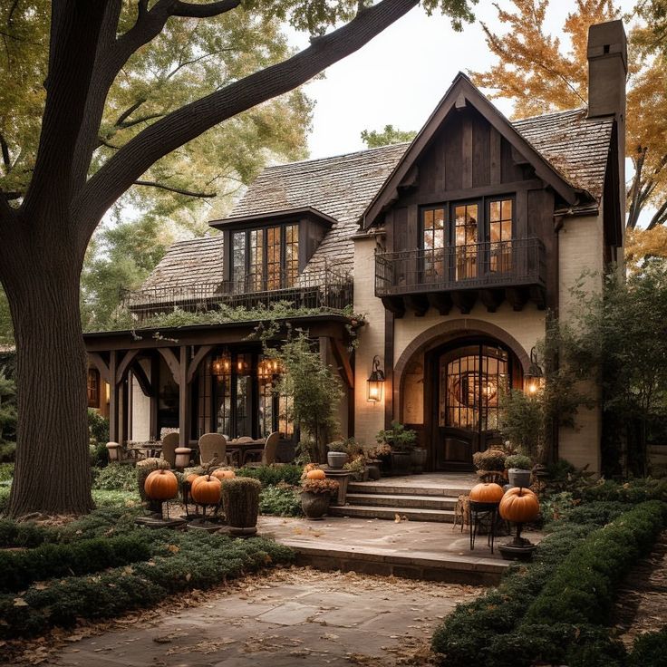 Tudor cottage with lit windows, stone path, pumpkins, and trees at dusk