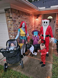 Family in Halloween costumes on residential porch including Sally, Jack Skellington, and children in various outfits