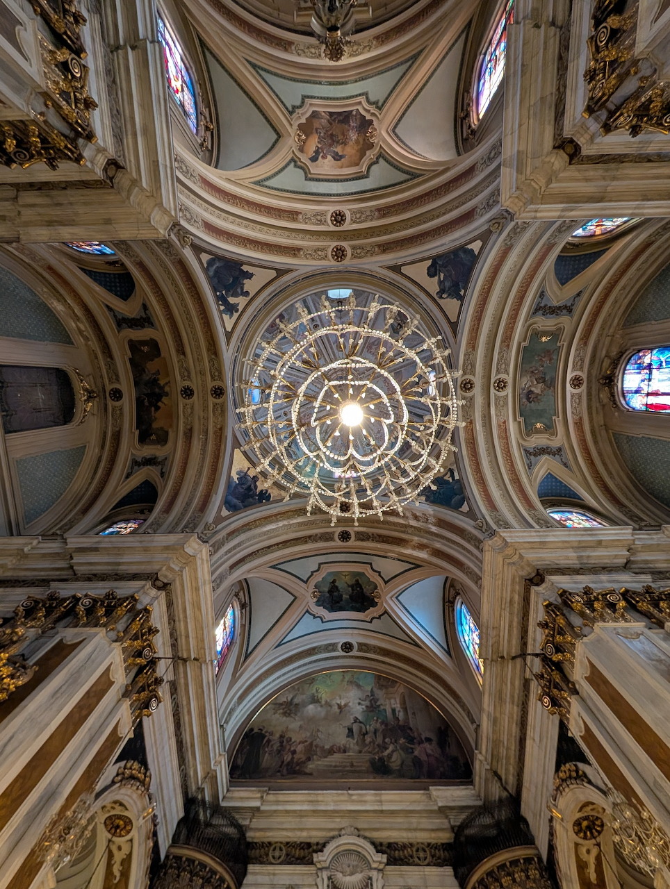 Upward view of ornate baroque church dome with concentric circles, arches, frescoes and stained glass windows