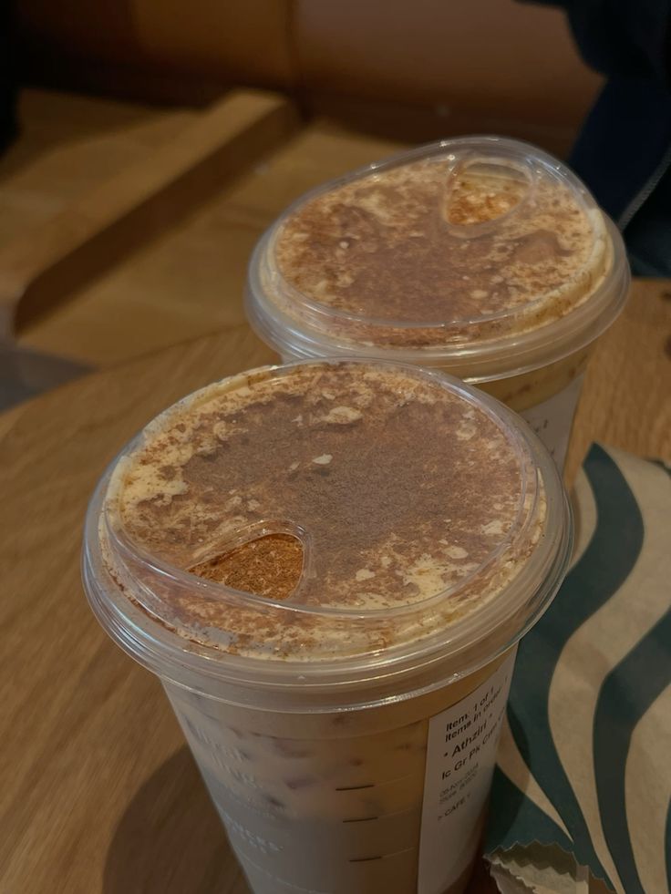 Two iced pumpkin spice lattes with cinnamon topping in plastic cups on wooden table