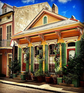 Colorful historic New Orleans house with green shutters, orange trim, front porch, and potted plants