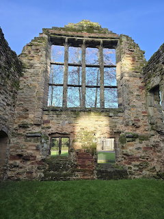 Ruined stone wall with a large window opening, blue sky, and grass below