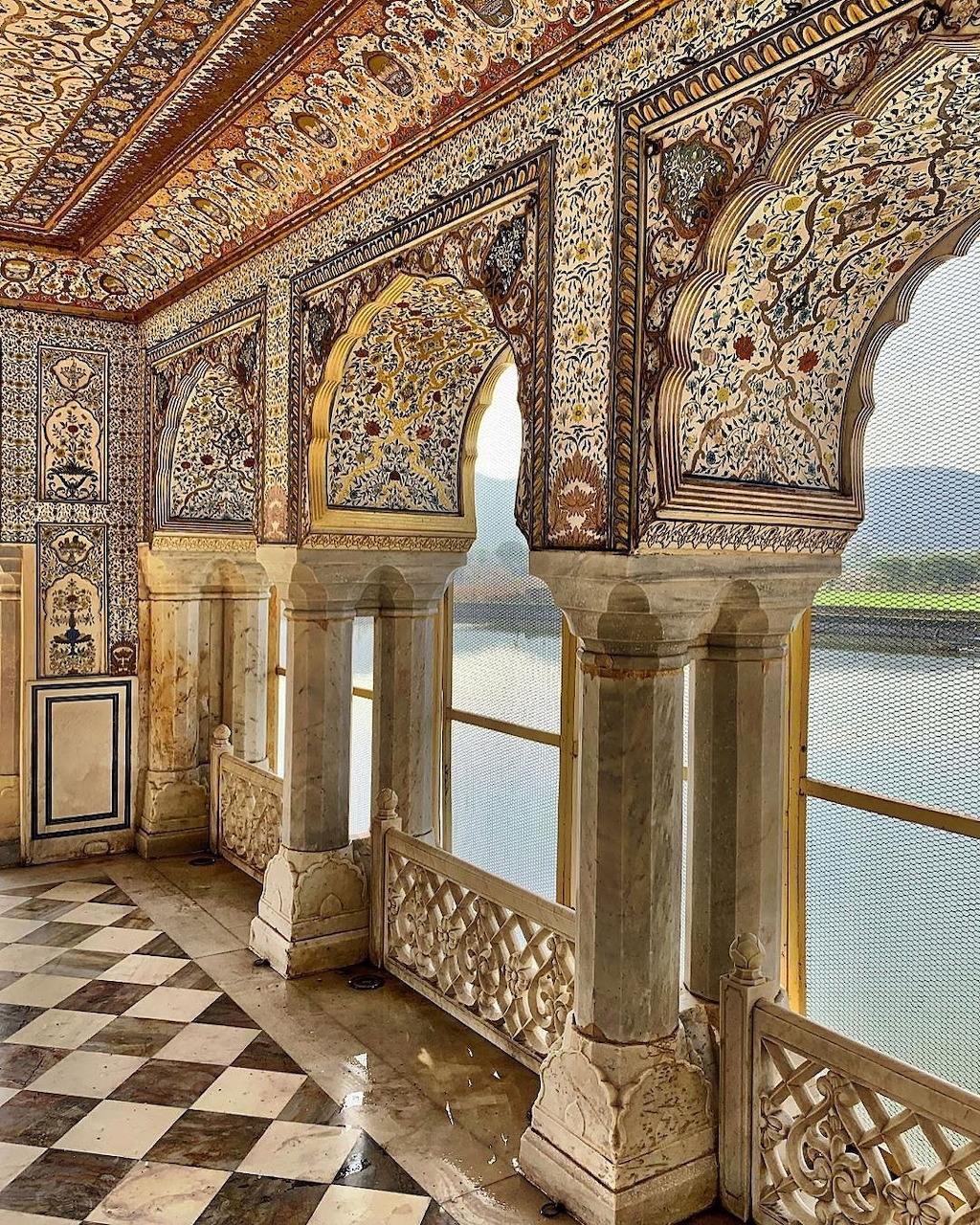 Ornate palace interior with decorated arches, frescoes, marble columns and checkered floor with lake view