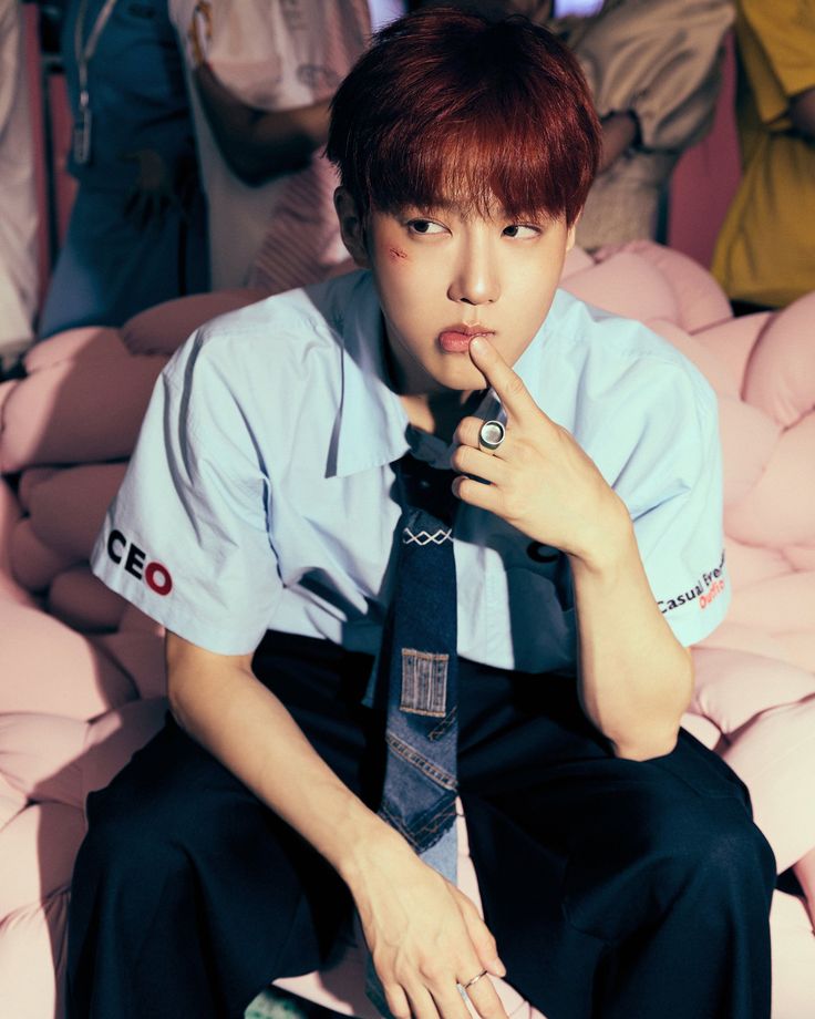 SUHO from EXO in light blue shirt and tie, hand near face, seated portrait