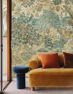 Living room with ornate floral wallpaper, mustard sofa, and black cylindrical table by window
