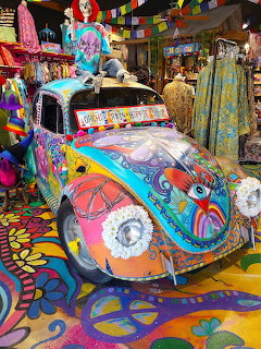 Brightly painted VW Beetle with colorful psychedelic designs in a hippie store with tie-dye clothing and decorations